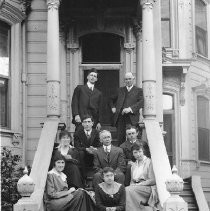 People seated on steps of a Victorian house