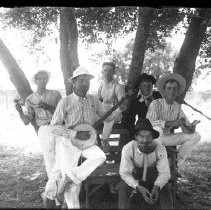 View of six musicians under a tree, eating watermelon