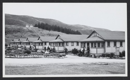 [view of barracks with detainees in front]