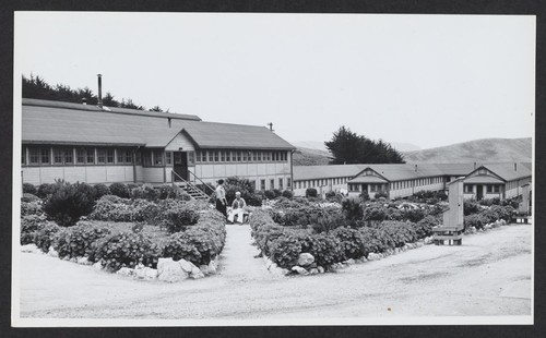 [barracks with gardens and 2 people sitting outside]