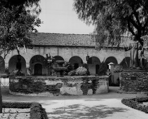 Two women in historical costumes stand in a courtyard of the San Fernando Mission