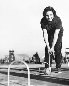 A woman poses for the camera as she prepares to stike a croquet ball in the middle of a Los Angeles playground
