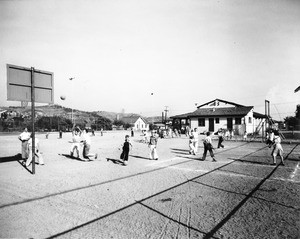 Many children playing various activites at the school playground, including basketball and four-square