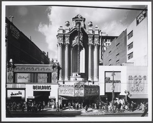 In Downtown Los Angeles, frontal view of the Los Angeles theatre showing Doself’s and Berland’s stores at left and Mode O’ Day and Mayson stores at right