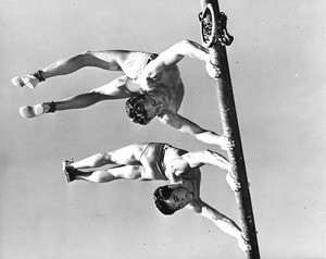 Two men practicing gymnastics from one of the playground bars