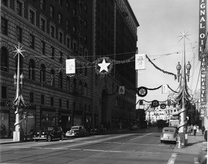 Seventh Street decorated for Christmas, looking west from the corner of Seventh Street and Flower Street, showing Signal Oil, Studebaker, and Pig 'n' Whistle Cafe signs