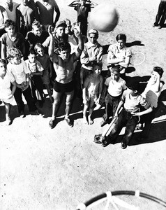 Many children watching as one student shoots some hoops at a school playground