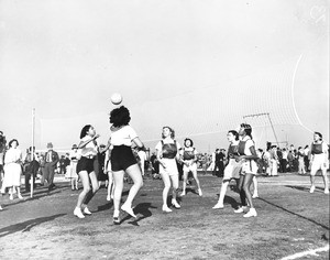 A group of women compete in a game of volleyball as many other people look on