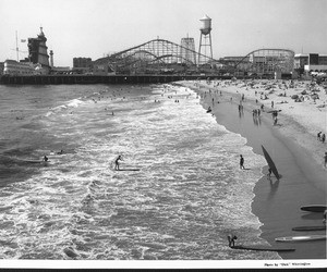 People crowd the beach next to an amusement park