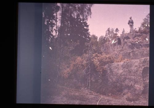 Photograph of man standing on rocky outcropping and looking away from camera