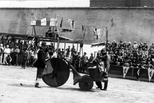 Entertainment featuring clowns with a handmade, high-wheeler tricycle, Scoreboard for Shops, Mills and Mess in the background, San Quentin Little Olympics Field Meet, 1930 [photograph]