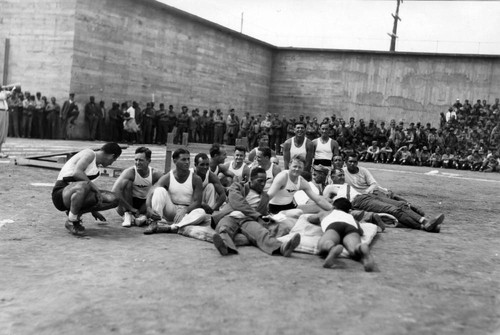 Prisoners and Olympic Club athletes sitting on the field during the tumbling competition, San Quentin Little Olympics Field Meet, 1930 [photograph]