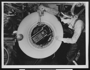 Factory worker manipulating a large white tire with machinery, ca.1930