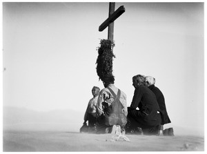 Four men kneeling before a cross at a funeral in the desert