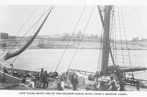 Men on a the deck of a shipping vessel showing Redondo Beach and Hotel in the distance, ca.1889