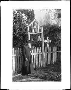 Father Pejol standing by the bells at Camulos ranch, ca.1892-1895