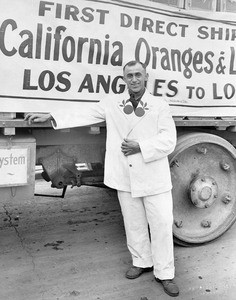 Portrait of a man standing in front of a sign advertising a historic orange shipment, ca.1920