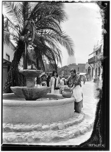 Two women by a fountain beneath a palm tree, possibly on Olvera Street