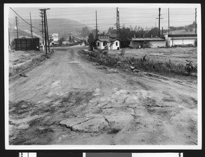 Oil seep interrupting pavement near buildings, ca.1930