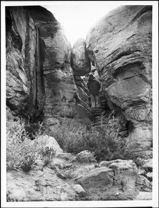 Man beneath a "fallen rock" on the foot trail to the top of Second Mesa and the pueblo of Mishongnovi (Mashongnavi), Arizona, ca.1898