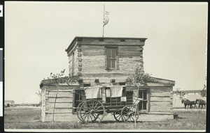 Cheyenne and Deadwood Stage in front of Jim Baker's house, brought in from its original site and placed in Cheyenne, Wyoming fairgrounds, ca.1929
