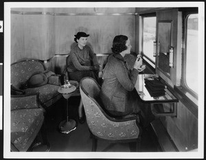 Two women, one of whom is putting on makeup at a mirror, in a new lightweight steel railroad car, ca.1930