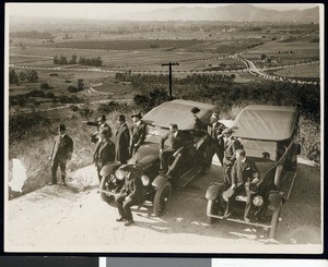 Two automobiles parked on a hill, with a group of men looking at the view, ca.1920