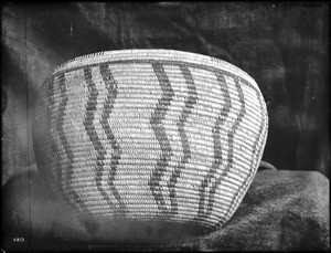 Indian basket displayed in front of a cloth backdrop, ca.1900