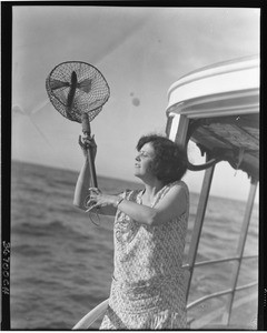 Woman catching a flying fish in a net from the deck of a boat