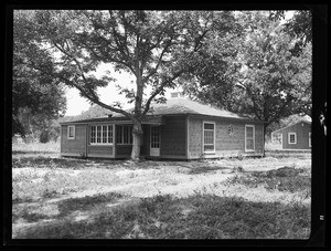 An exterior view of a one-story house, showing a second house in the back