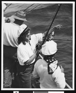 Woman landing a calico bass from a fishing boat, off San Clemente, ca.1930