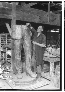 Sculptor putting the finishing touches on the bottom half of a statue of a man