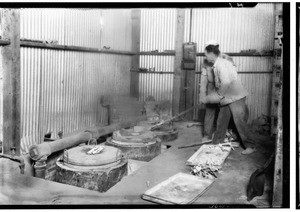 Men moving small metal bricks with a long set of tongs