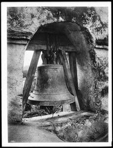 Close-up of the largest bell in the bell tower of Mission San Gabriel, ca.1900
