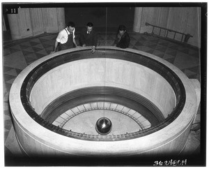 Three men inspecting a large pendulum in the Griffith Park Observatory lobby, ca.1930-1950