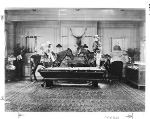Two men playing a game of pool on horseback inside the home of Eugene Plummer, ca.1920