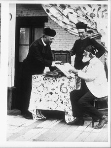 Two Los Angeles Plaza church priests with Don Antonio Coronel examining church records, ca.1885-1900