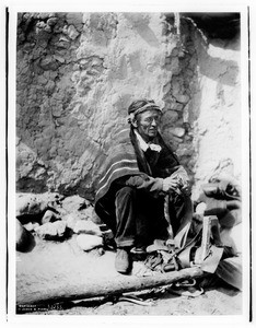 Navajo Indian saddler sitting in front of an adobe dwelling, ca.1901