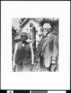 Jose de los Gantos (Gatos?) and Charles Prudhomme standing before a house and a barbed wire fence, ca.1931