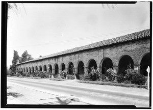 Exterior view of a long mission building, showing a street