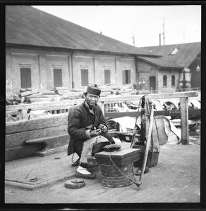 Sheet merchant and shoe maker sitting on the docks in China, ca.1900