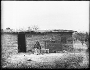 Mrs. Scott, a Christian Indian woman "educated by the white man", sitting in front of her native dwelling, ca.1900