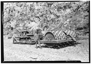 Man standing with a tractor at the construction of the San Gabriel Dam, 1936