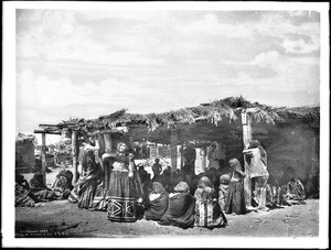 Group of Mojave Indians mourning over the body of their dead chief, Sistuma, in front of a small dwelling with a thatched roof, ca.1902