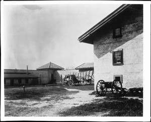 Courtyard at Sutter's Fort showing a stage coach, a wagon and a cannon, ca.1900