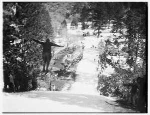 Ski jumper spreading his arms as he leaps down a mountain slope, while a crowd watches