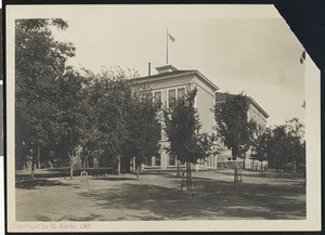 Exterior view of what appears to be a school-house hidden behind tree foilage, ca.1907