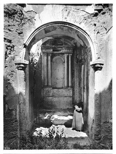 Father Superior O'Keefe standing in the ruins of the mortuary chapel of Mission San Luis Rey de Francia, California, 1904