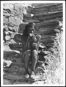 Old Hopi Indian man sitting on stone steps in the village of Shonguapavi, ca.1901