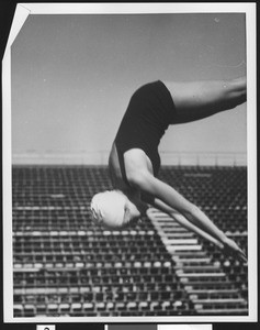 Female diver in mid-air with a grandstand behind her, ca.1930